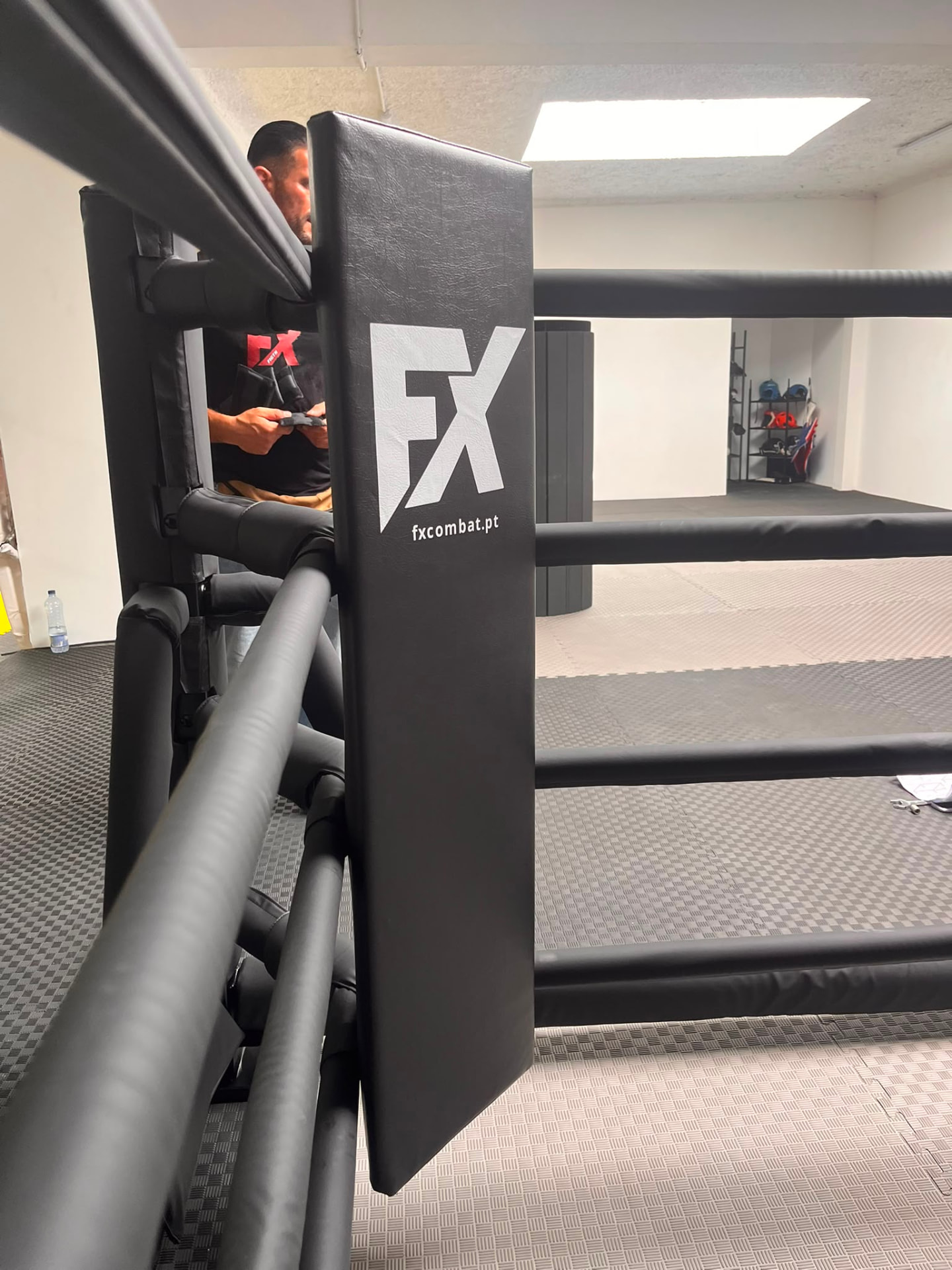Ringue FX de chão com proteções pretas e logótipo FX numa sala de treino